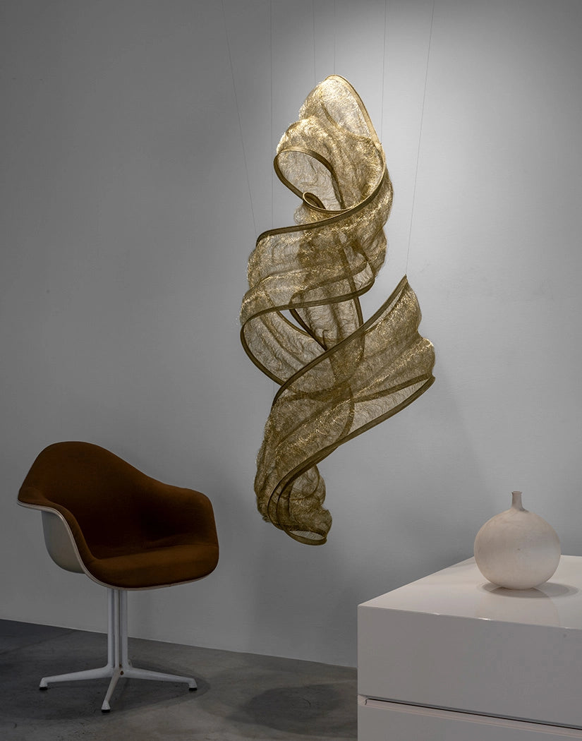 Genesis Vertical Floating Knit Sculpture by Terzani in brass, suspended in a minimalist workspace.